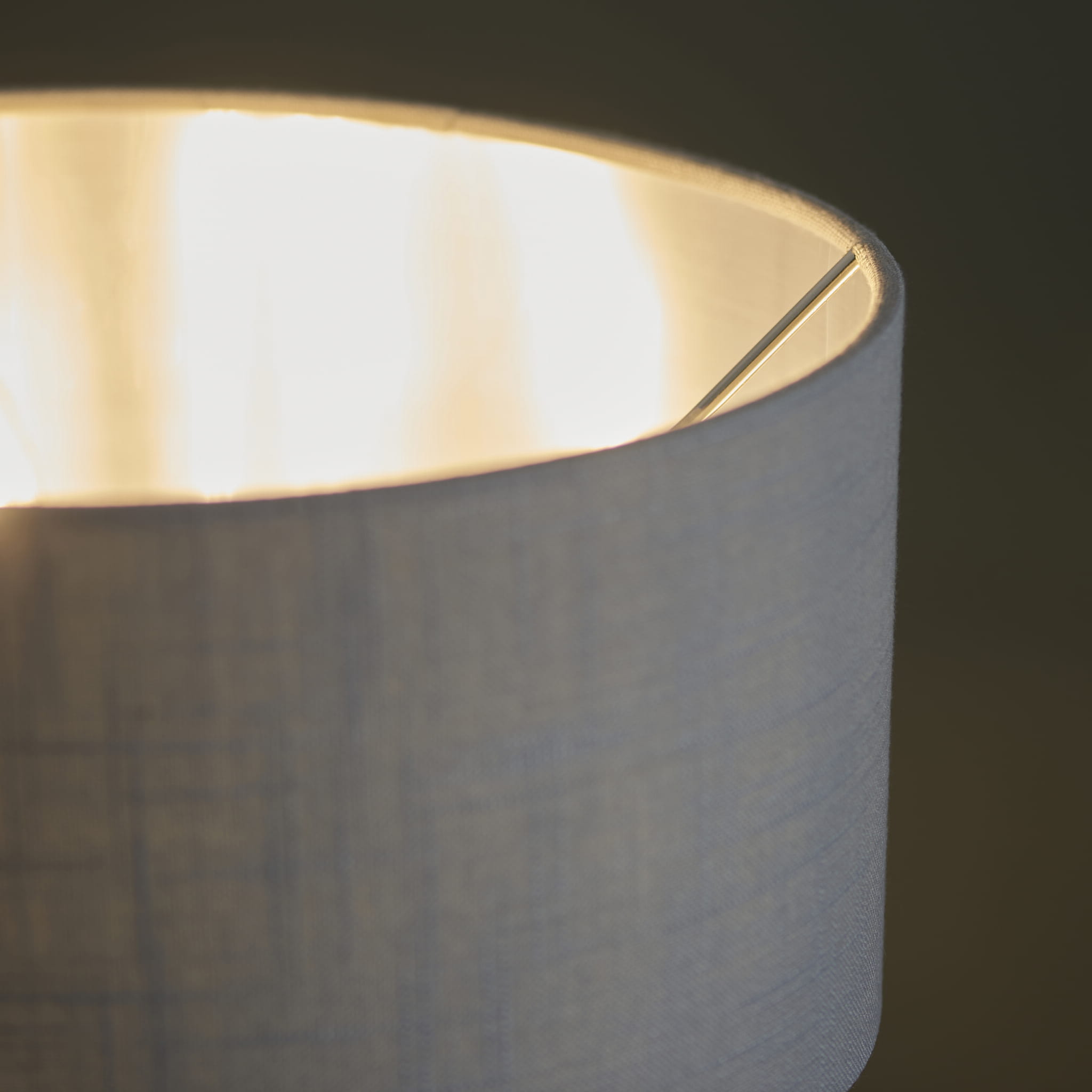 Lampa stołowa Highclere w kolorze szarym, wysokość 50 cm, z teksturowanym abażurem. Ujęcie z bliska, ukazujące górną część lampy oraz źródło światła. Metalowy element mocujący wewnątrz. Tło ciemne, podkreślające detale produktu.