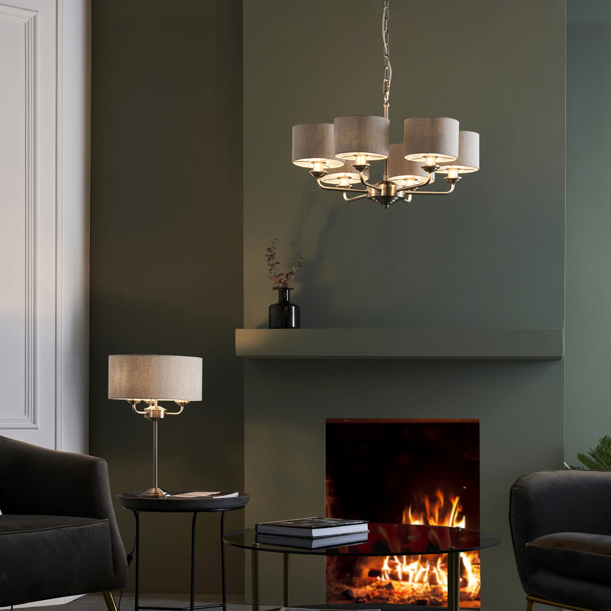 Lampa sufitowa wisząca Highclere w kolorze chromu z sześcioma szarymi abażurami. Produkt zamontowany w aranżacji wnętrza z paleniskiem w tle. Kąt ujęcia frontalny, ukazujący elegancki design oraz materiałowe abażury.
