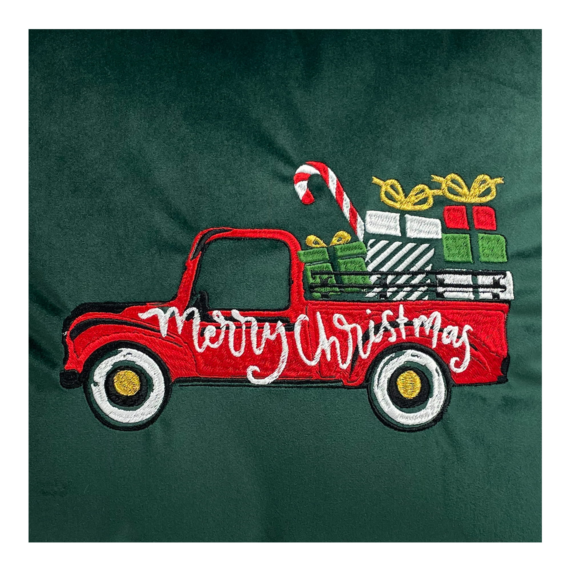 Poduszka haftowana w kształcie czerwonego samochodu z prezentami i ozdobami w kolorze zielonym. Haft zawiera napis Merry Christmas oraz detale jak biały cukierek i prezenty w różnych kolorach. Produkt leży na jednolitym tle.