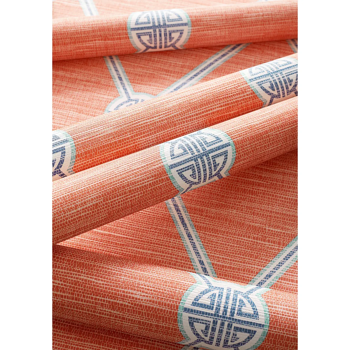 Tapeta Thibaut Anna French TURNBERRY TRELLIS w kolorze koralowym, z niebieskimi detalami. Wzór siatki i okręgów umieszczony na fakturze w stylu płótna. Produkt leży na stole, odsłaniając ułożone pasy materiału z wyraźnymi liniami i geometrą.