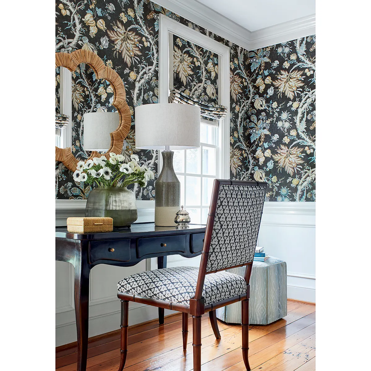 Tapeta Thibaut Anny French CHATELAIN w zielonym kolorze z delikatnym wzorem roślinnym na ciemnym tle. Ujęcie mostra produkt na ścianie w jasnym wnętrzu z meblem i lampą. W tle widoczny stół z wazonem i kwiatami.