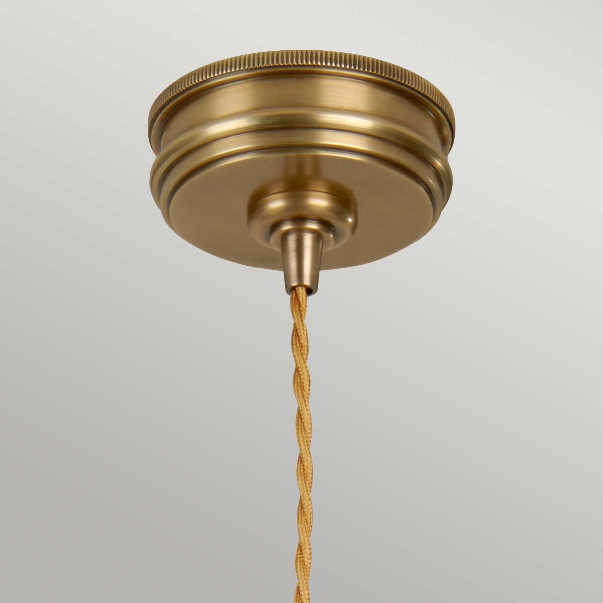 Mosiężna lampa wisząca Ravello z czaszą w kolorze złotym. Widok z dołu, ukazujący detal mocowania oraz pleciony kabel w odcieniu beżowym. Tło jednolite, co podkreśla elegancję produktu.