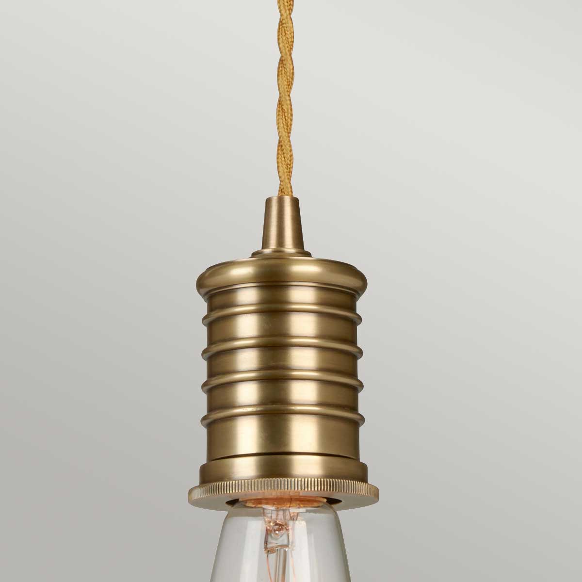 Lampa wisząca Ravello w kolorze mosiądzu, z okrągłym, teksturowanym uchwytem oraz przezroczystym kloszem. Ujęcie frontalne, produkt jest zamontowany na zernej, plecionej lince. Tło jest jednolite, co podkreśla detale lampy.