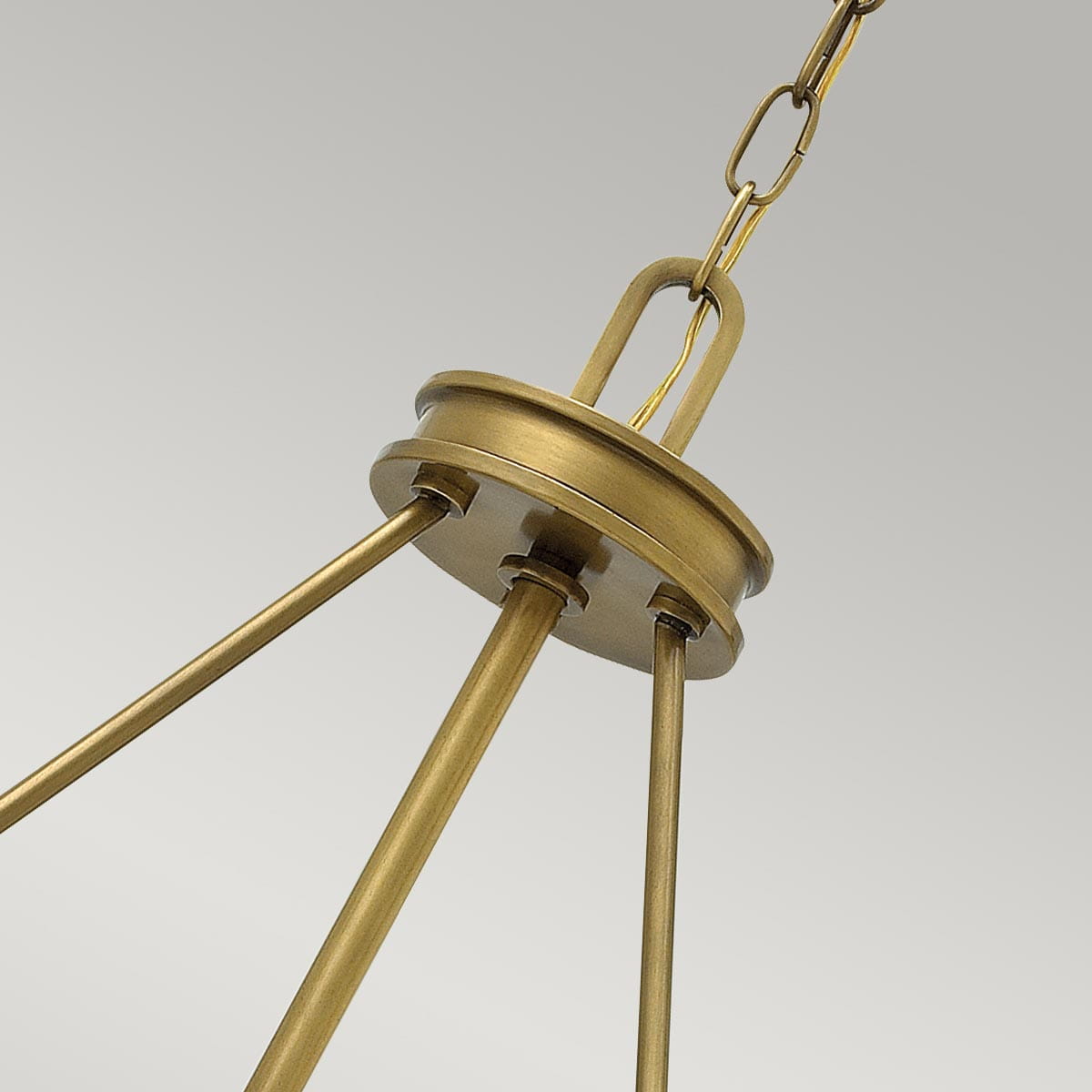 Lampa wisząca Aurea w kolorze stary mosiądz. Widok z dołu, ukazuje detal mocowania i łańcucha. Produkt ma trzy metalowe ramiona, które łączą się w centralnym elemencie. Tło w jasnoszarym odcieniu, co podkreśla kolorystykę lampy.